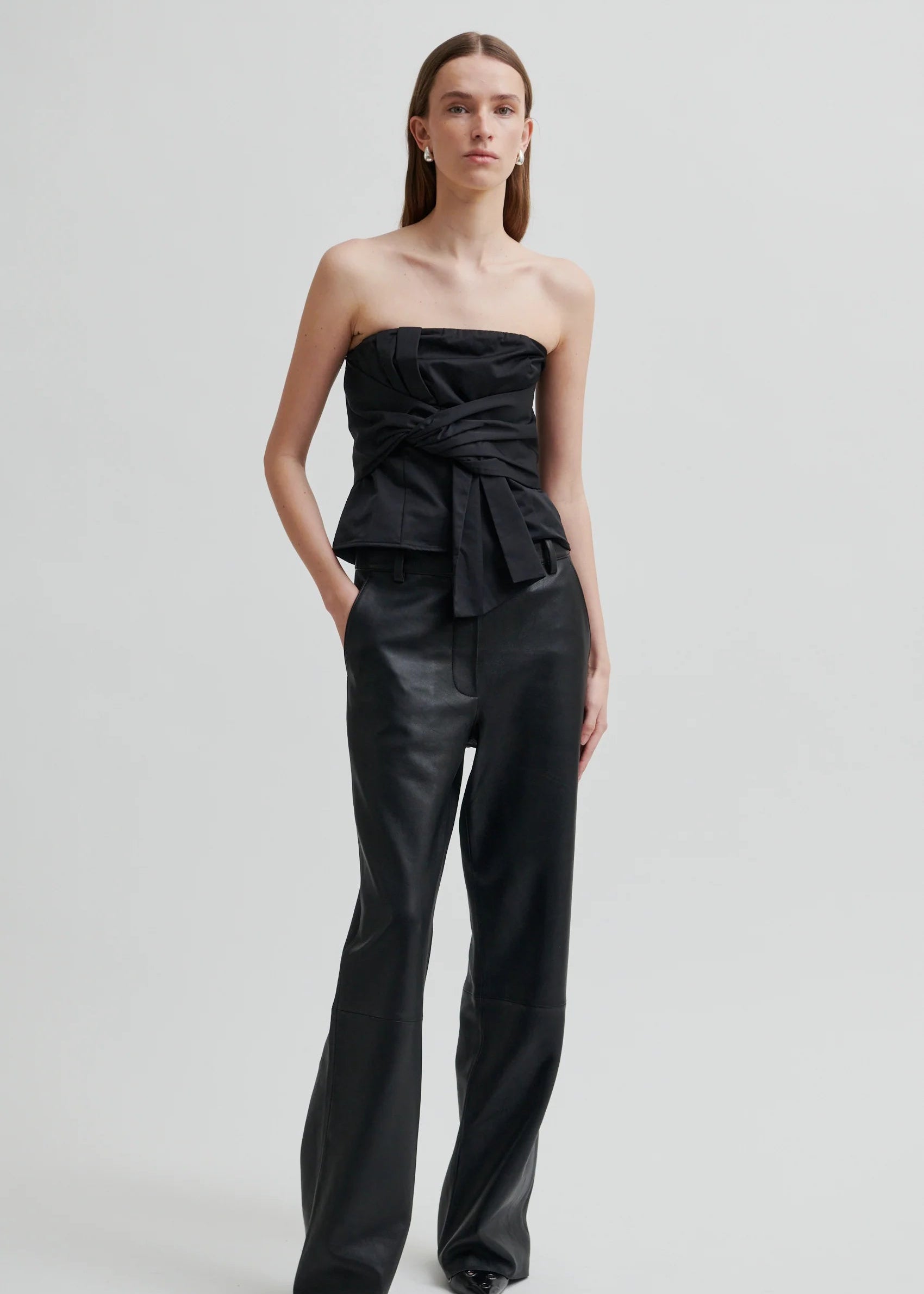Woman wearing a black strapless top and black pants on a light grey background