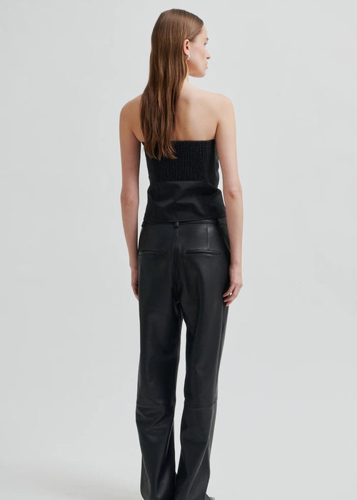 Woman wearing a black strapless top and black pants on a light grey background