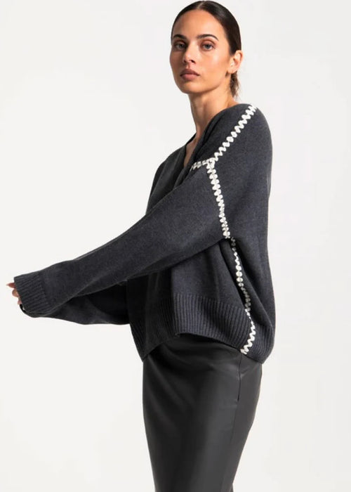 Woman wearing a dark grey sweater with white trim on a plain background