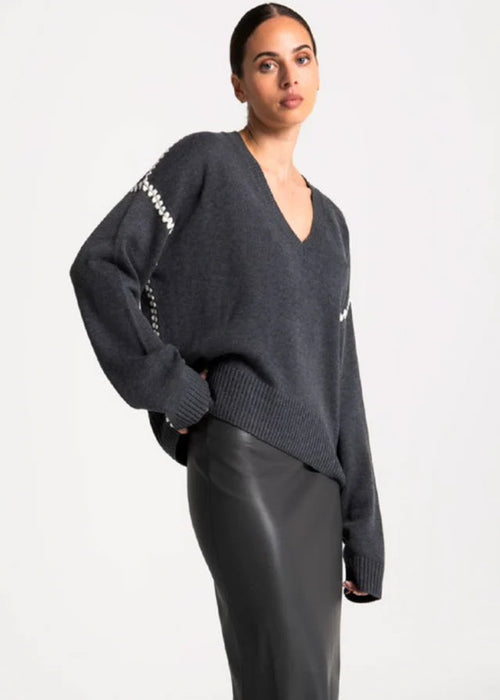 Woman wearing a dark grey sweater with white trim on a plain background
