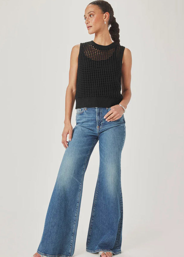Woman wearing a black sleeveless knitted top and blue jeans on a plain background