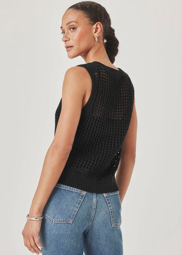 Woman wearing a black sleeveless knitted top and blue jeans on a plain background
