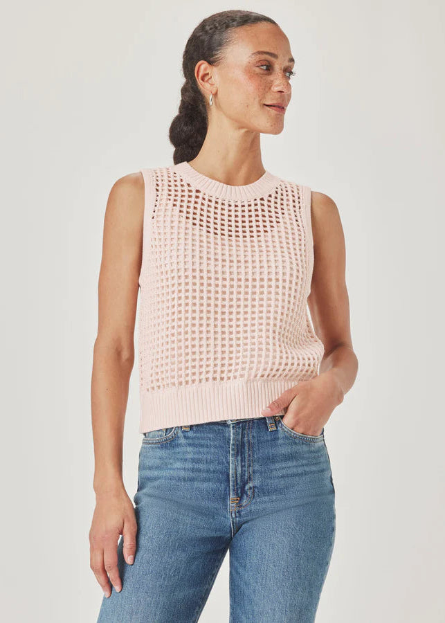 Woman wearing a light pink sleeveless knitted top and blue jeans on a plain background