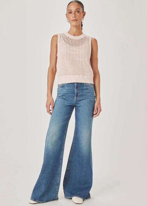 Woman wearing a light pink sleeveless knitted top and blue jeans on a plain background