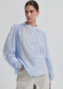 Woman wearing a light blue blouse with intricate patterns on a plain background
