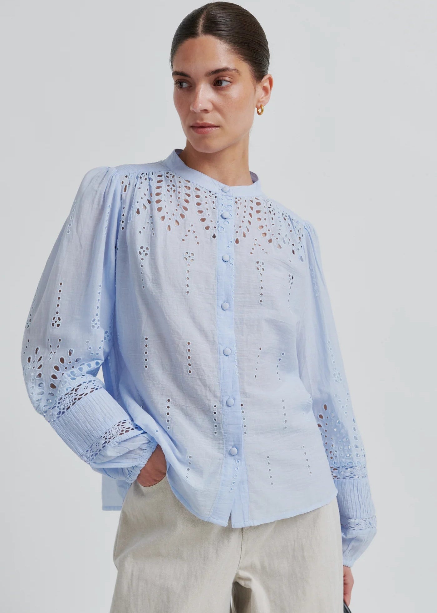 Woman wearing a light blue blouse with intricate patterns on a plain background