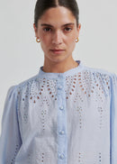 Woman wearing a light blue blouse with intricate patterns on a plain background