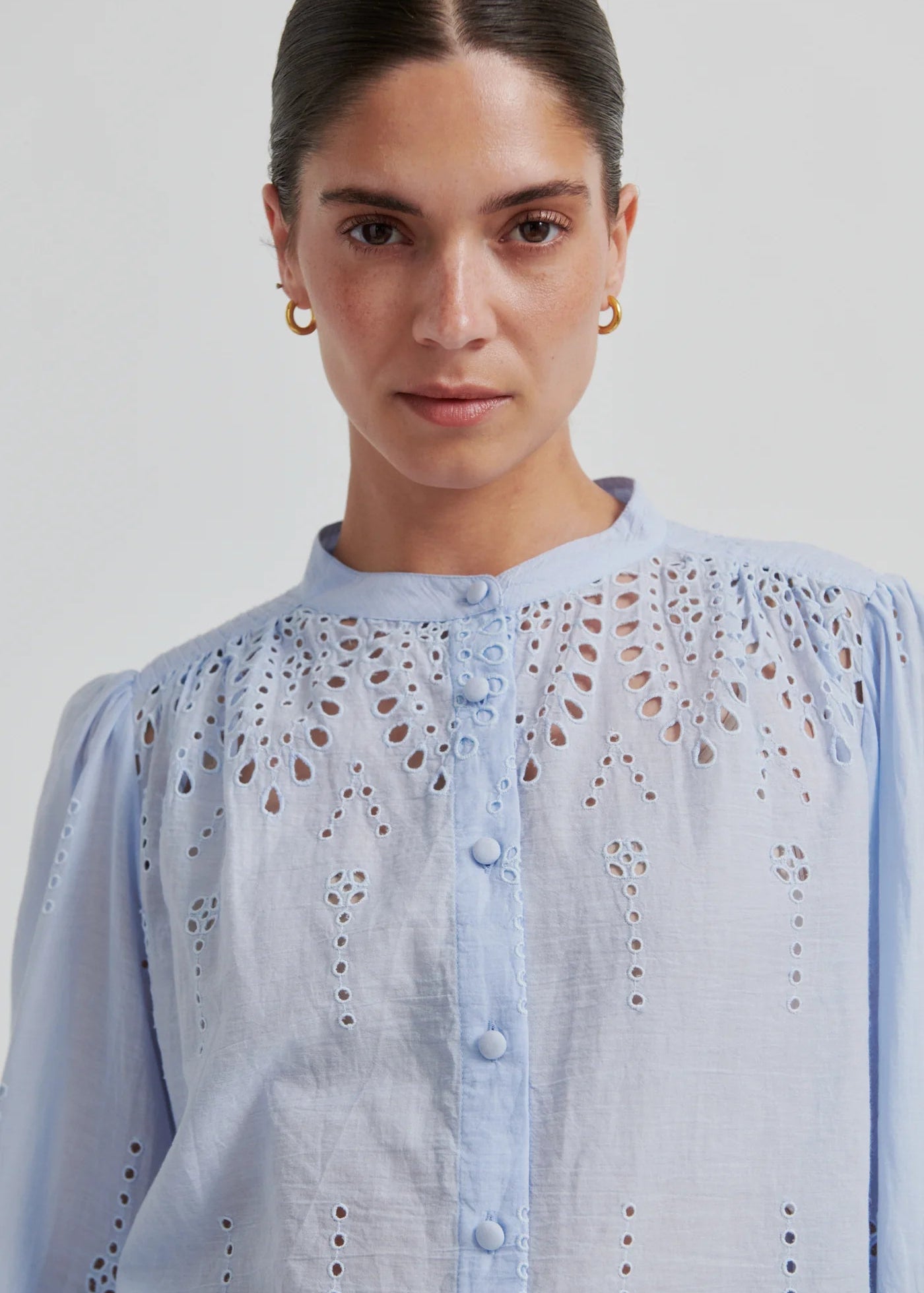 Woman wearing a light blue blouse with intricate patterns on a plain background