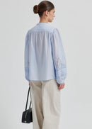 Woman wearing a light blue blouse with intricate patterns on a plain background