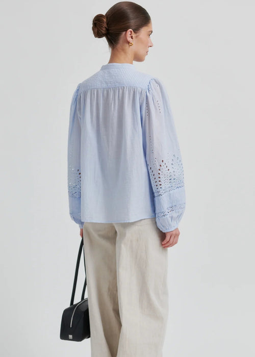 Woman wearing a light blue blouse with intricate patterns on a plain background