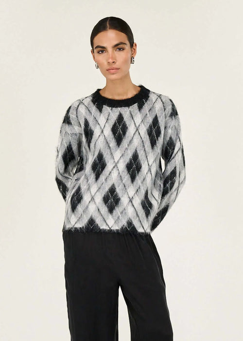 Woman wearing a patterned sweater and black pants on a white background