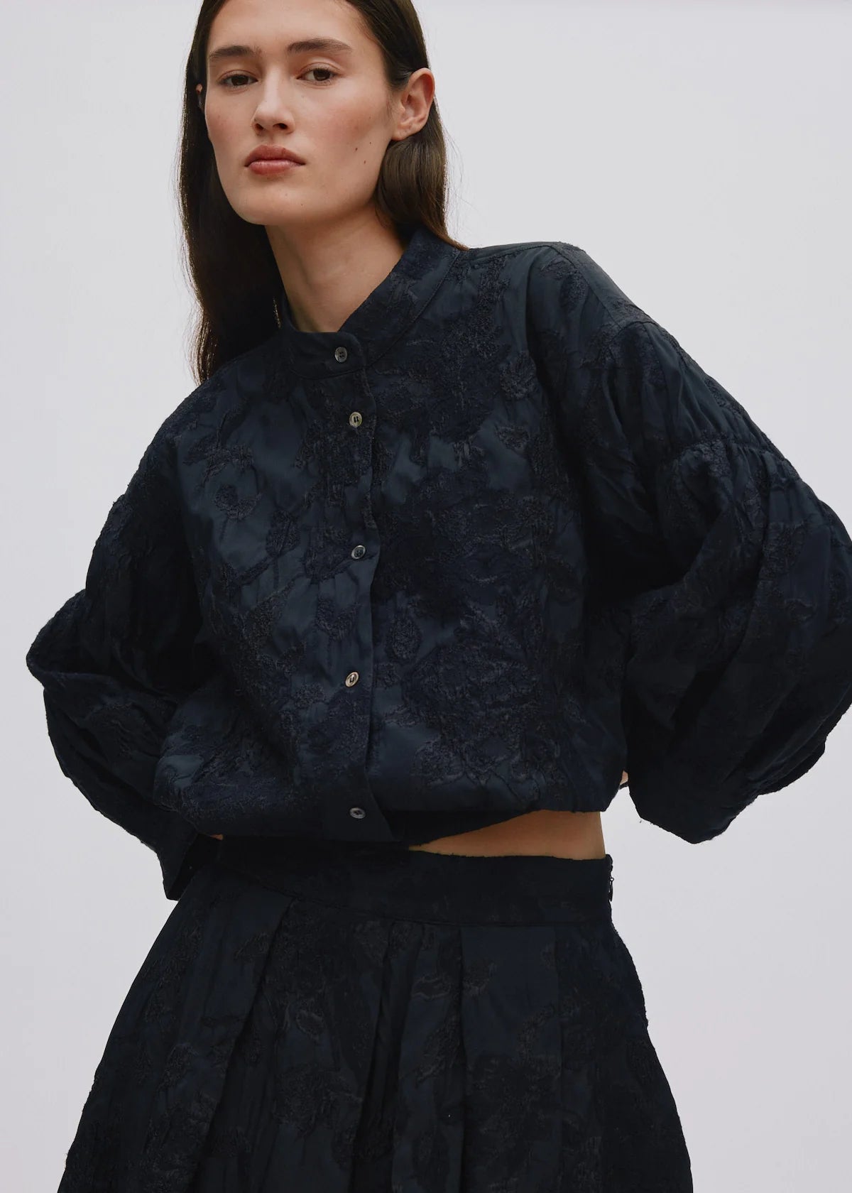 Woman wearing black textured blouse with button details on a white background