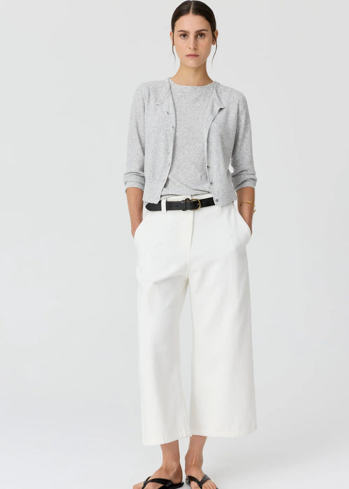 A woman modelling a light grey cardigan over a matching grey top, paired with white cropped trousers, a black belt, and black sandals, against a plain light grey studio background.