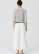 A woman modelling a light grey cardigan over a matching grey top, paired with white cropped trousers, a black belt, and black sandals, against a plain light grey studio background.