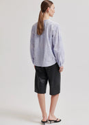 A model wearing a light lavender long-sleeve blouse with textured floral embroidery and a button-up front, paired with black leather pants