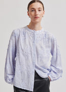A model wearing a light lavender long-sleeve blouse with textured floral embroidery and a button-up front, paired with black leather pants