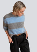 Woman wearing a striped sweater with grey and blue colours on a plain background