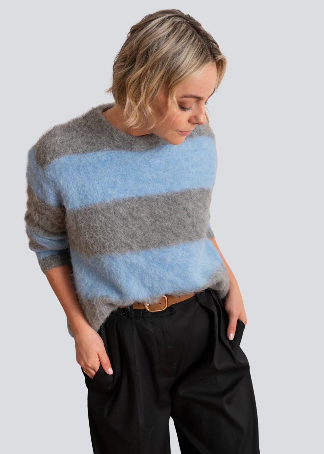 Woman wearing a striped sweater with grey and blue colours on a plain background