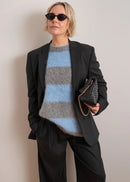 Woman wearing a striped sweater with grey and blue colours on a plain background