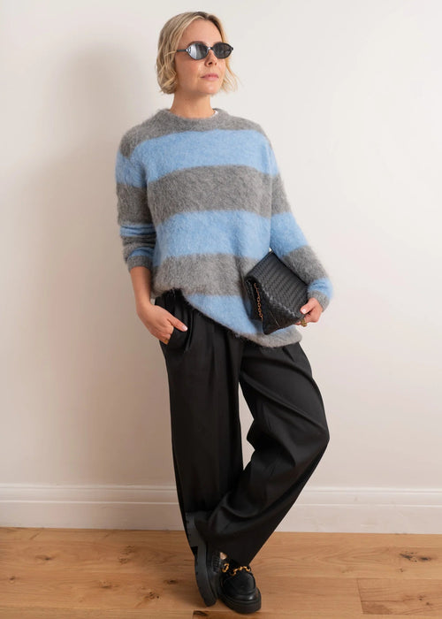 Woman wearing a striped sweater with grey and blue colours on a plain background