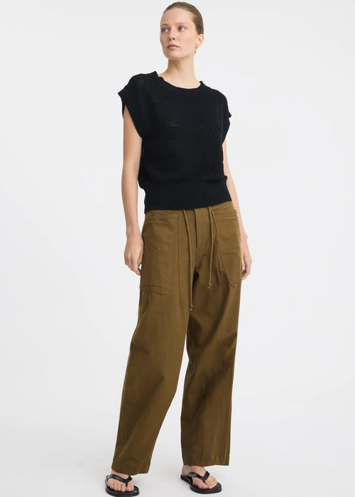 A model wearing a black sleeveless knit top and olive green wide-leg pants with a drawstring waist, paired with black sandals, against a plain white studio background.