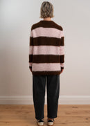 Woman wearing a brown and pink striped sweater with black pants and sneakers on a plain background