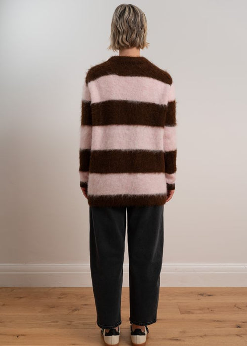Woman wearing a brown and pink striped sweater with black pants and sneakers on a plain background