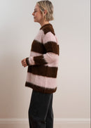 Woman wearing a brown and pink striped sweater with black pants and sneakers on a plain background