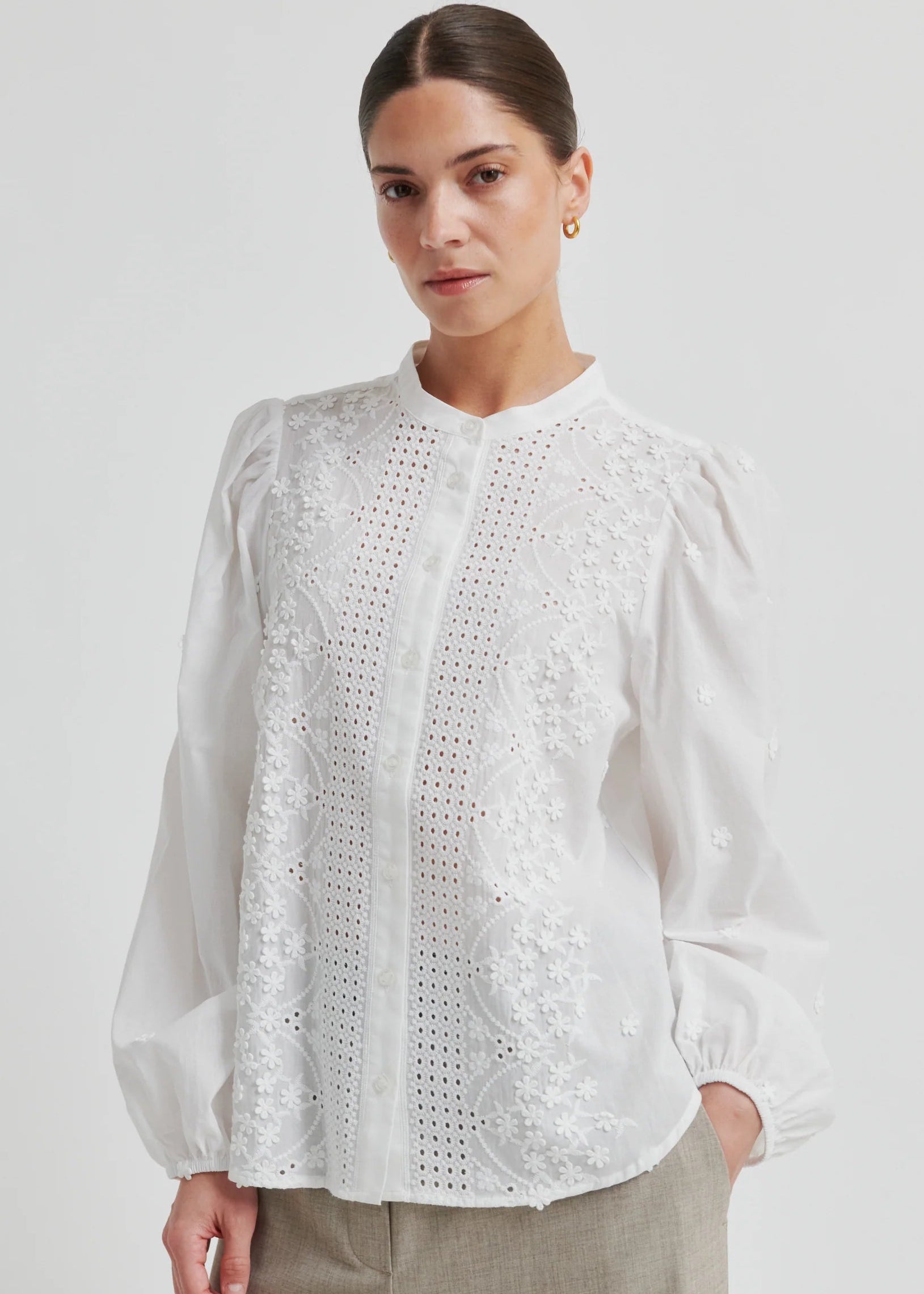 Woman wearing a white blouse with intricate patterns on a plain background