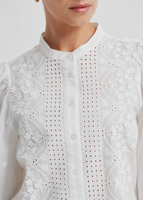Woman wearing a white blouse with intricate patterns on a plain background