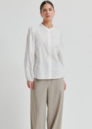 Woman wearing a white blouse with intricate patterns on a plain background