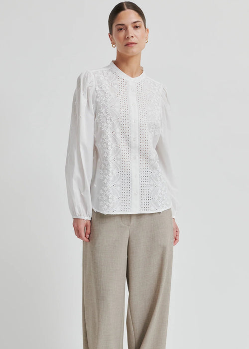 Woman wearing a white blouse with intricate patterns on a plain background