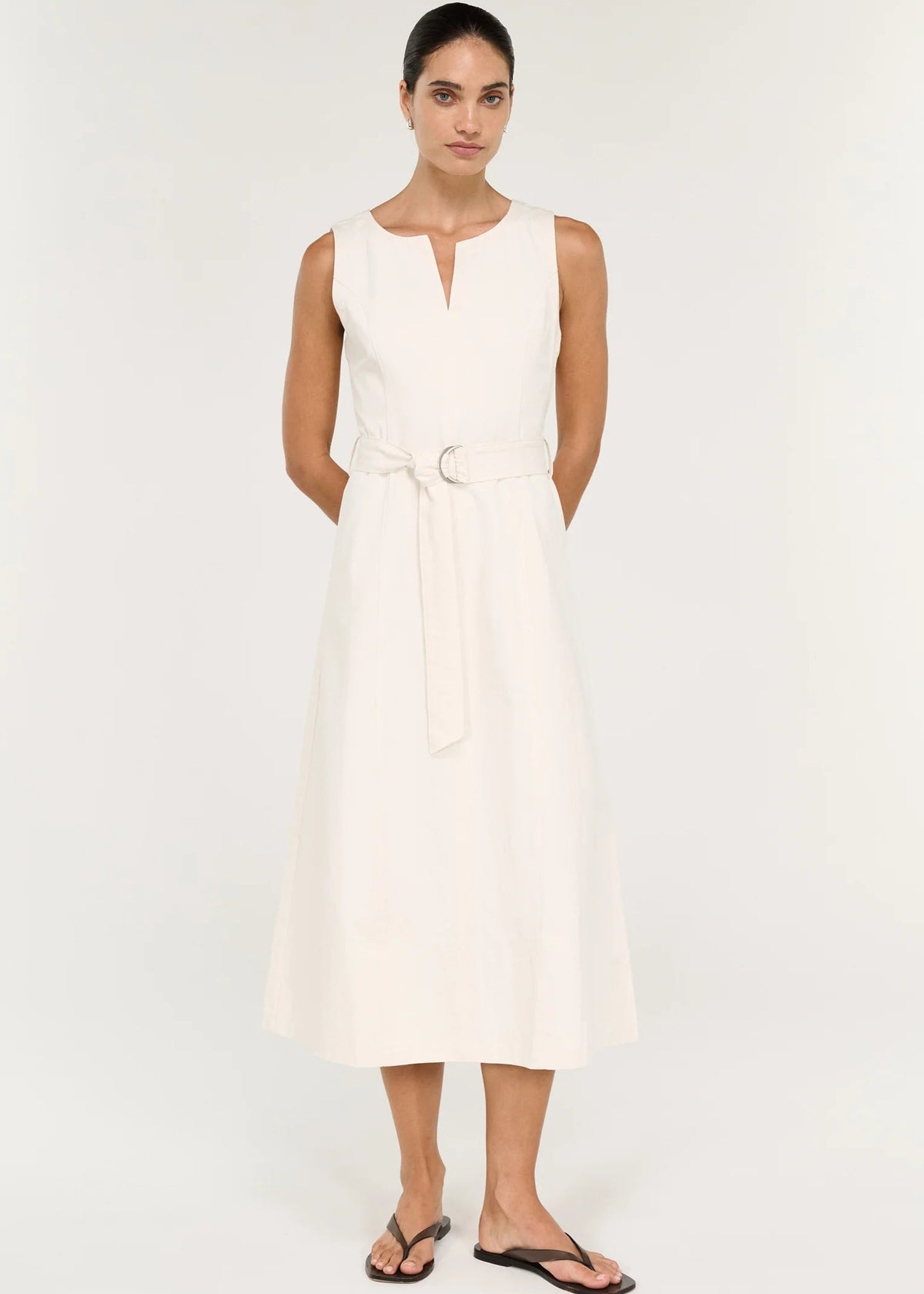 A woman modelling a sleeveless white dress with a keyhole neckline and a matching waist tie belt, photographed against a plain light background.