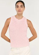 A woman modelling a light pink sleeveless knit top with white trousers, standing against a plain white studio background.