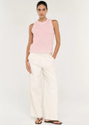 A woman modelling a light pink sleeveless knit top with white trousers, standing against a plain white studio background.
