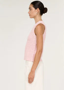 A woman modelling a light pink sleeveless knit top with white trousers, standing against a plain white studio background.