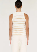 A woman modelling a sleeveless knit top with horizontal beige stripes on a white textured background, paired with white trousers, against a light grey studio backdrop.