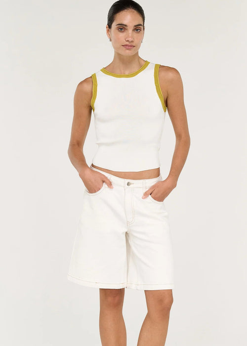A woman modelling a white ribbed knit sleeveless crop top with yellow trim and white denim shorts against a plain light background.