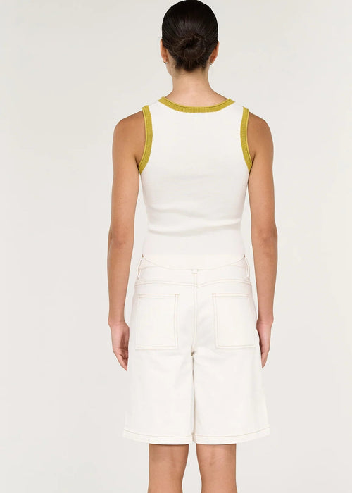 A woman modelling a white ribbed knit sleeveless crop top with yellow trim and white denim shorts against a plain light background.