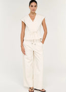 A woman modelling a cream-colored wrap-style top with a tie waist and matching wide-leg pants against a plain white studio background.
