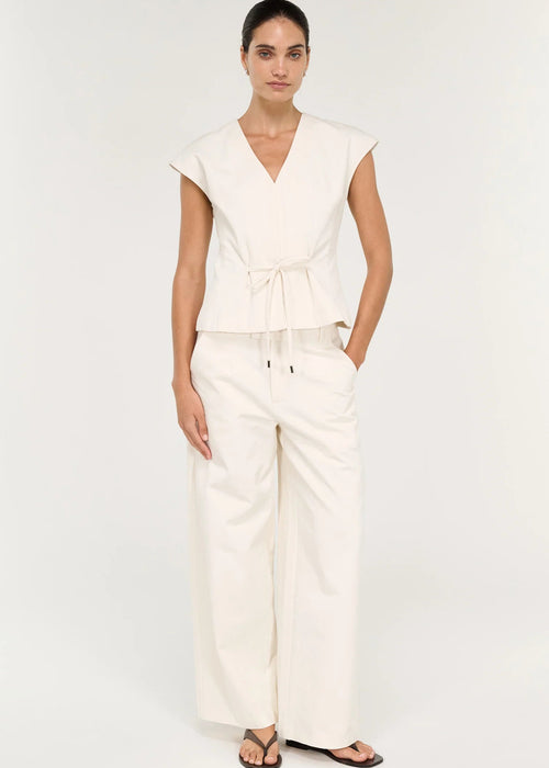 A woman modelling a cream-colored wrap-style top with a tie waist and matching wide-leg pants against a plain white studio background.