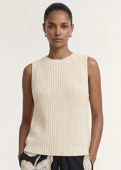 A woman modeling a sleeveless cream-colored ribbed knit top paired with black floral pants against a plain light background.