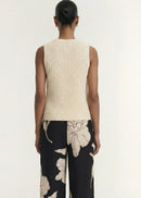 A woman modelling a sleeveless cream-colored ribbed knit top paired with black floral pants against a plain light background.