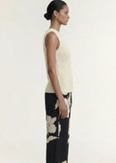 A woman modelling a sleeveless cream-colored ribbed knit top paired with black floral pants against a plain light background.