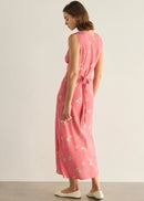 A woman modelling a sleeveless pink midi dress with a delicate white and green floral print, standing against a neutral light grey studio background.
