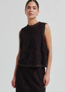 Woman wearing a black sleeveless lace top against a plain background