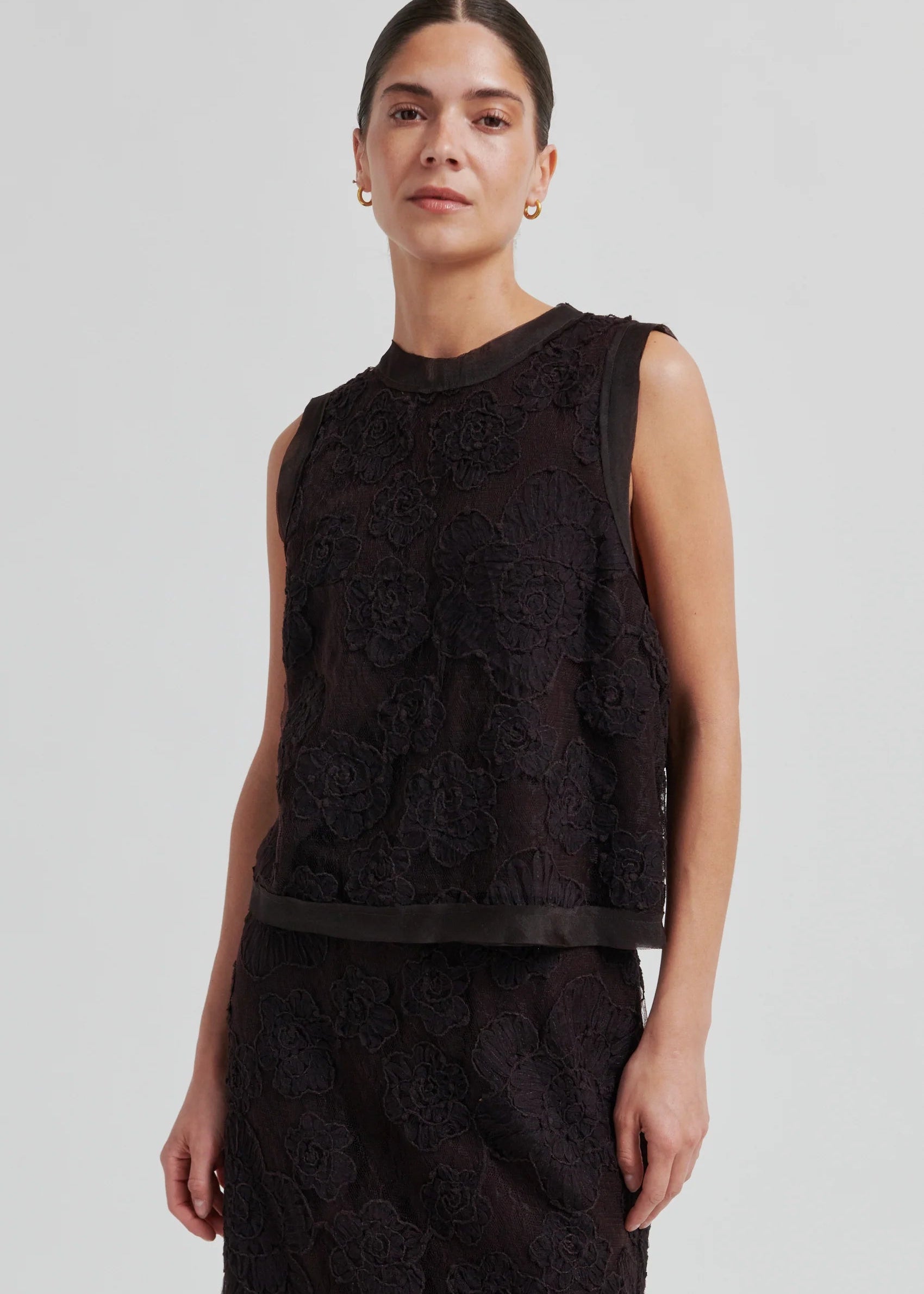 Woman wearing a black sleeveless lace top against a plain background