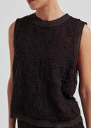 Woman wearing a black sleeveless lace top against a plain background