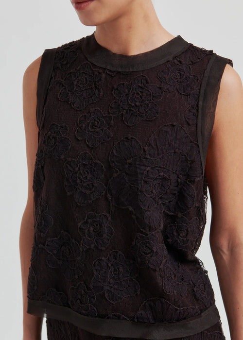 Woman wearing a black sleeveless lace top against a plain background