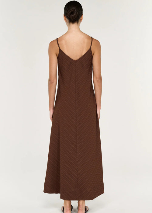 Woman modelling a sleeveless brown maxi dress on grey background viewed from behind